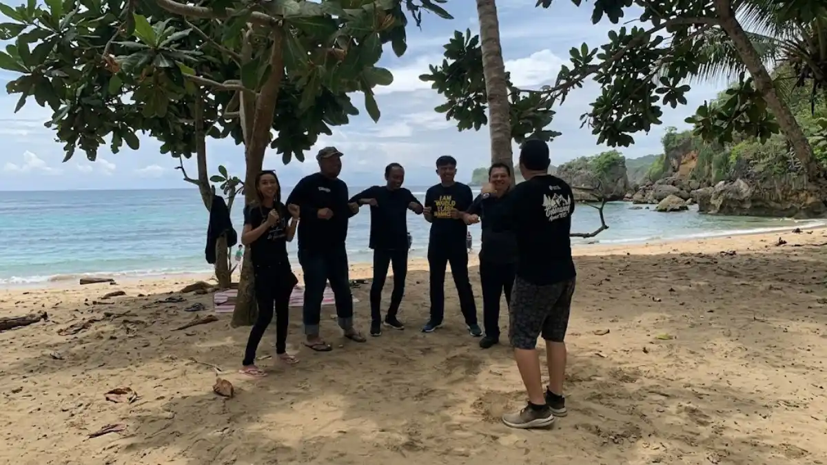 Karyawan berkumpul untuk gathering pagi di pantai saat matahari terbit